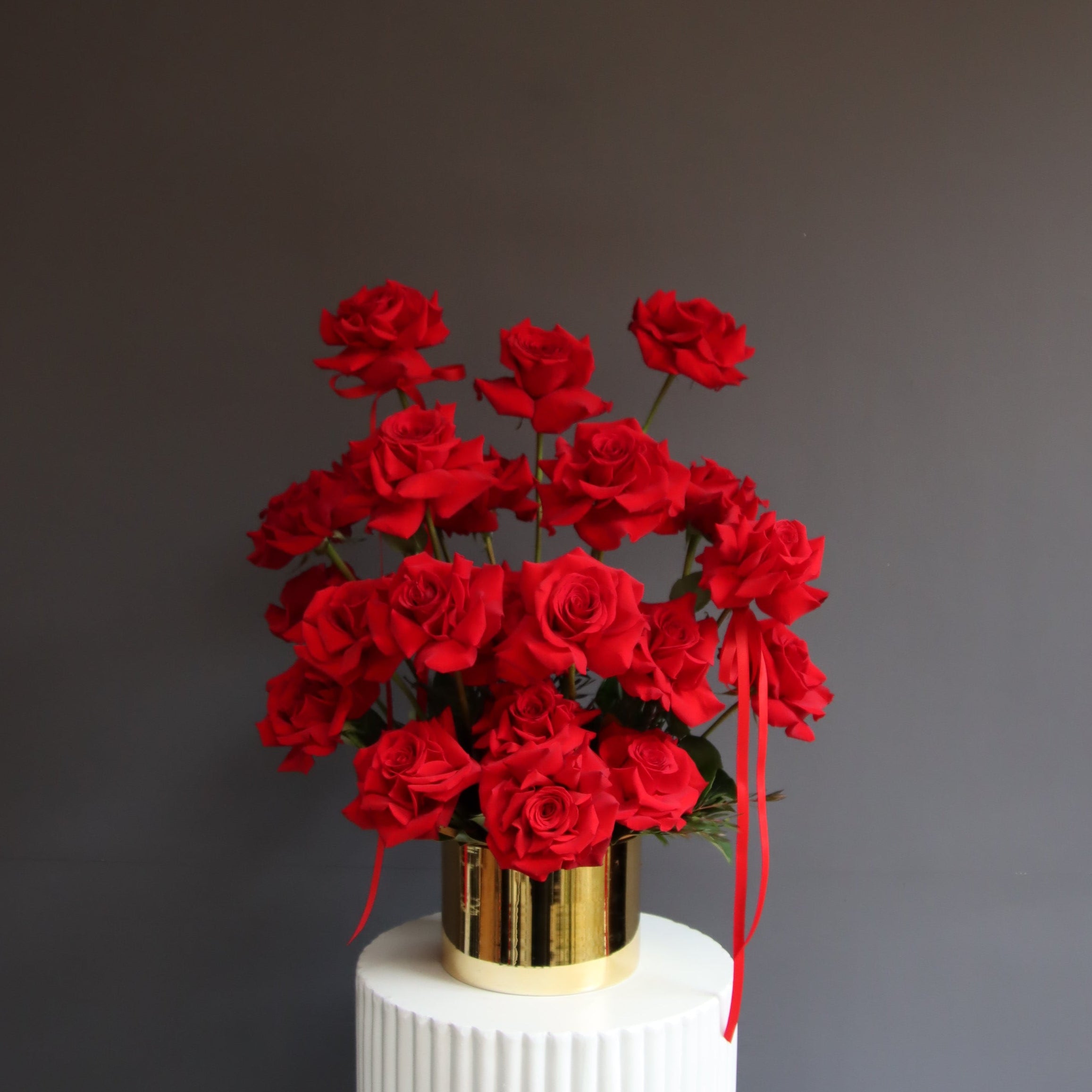 Red reflexed roses arranged in a gold glass pot
