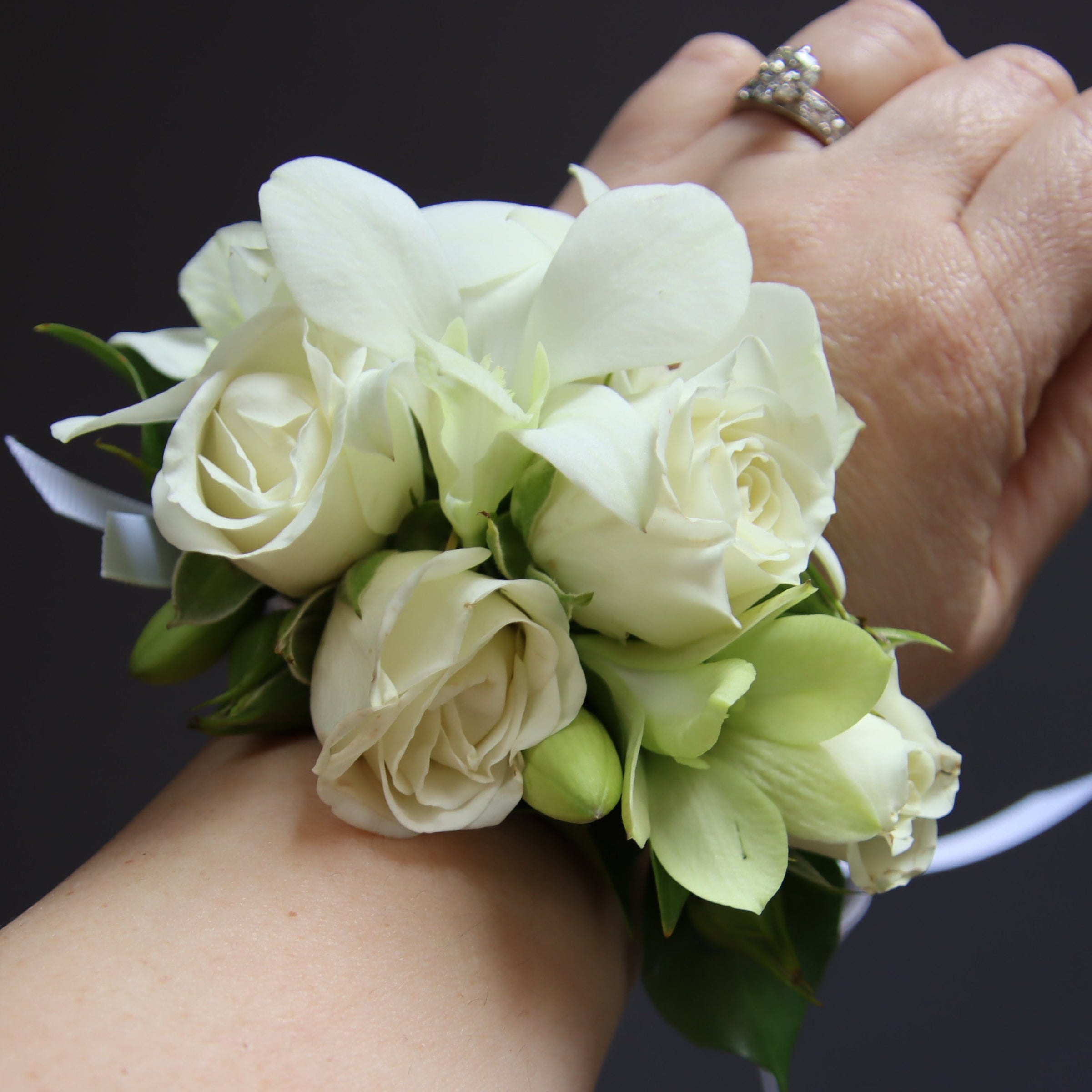 Our classic delicate fully wired wrist corsage features white spray roses and white dendrobium orchids with buds, accented with minimal greenery and ribbons. The wired design wraps securely around the wrist like a watch, ensuring it stays in place throughout your event. Ideal for weddings, formals, and special occasions. Available in a range of colors to complement your outfit or event theme.