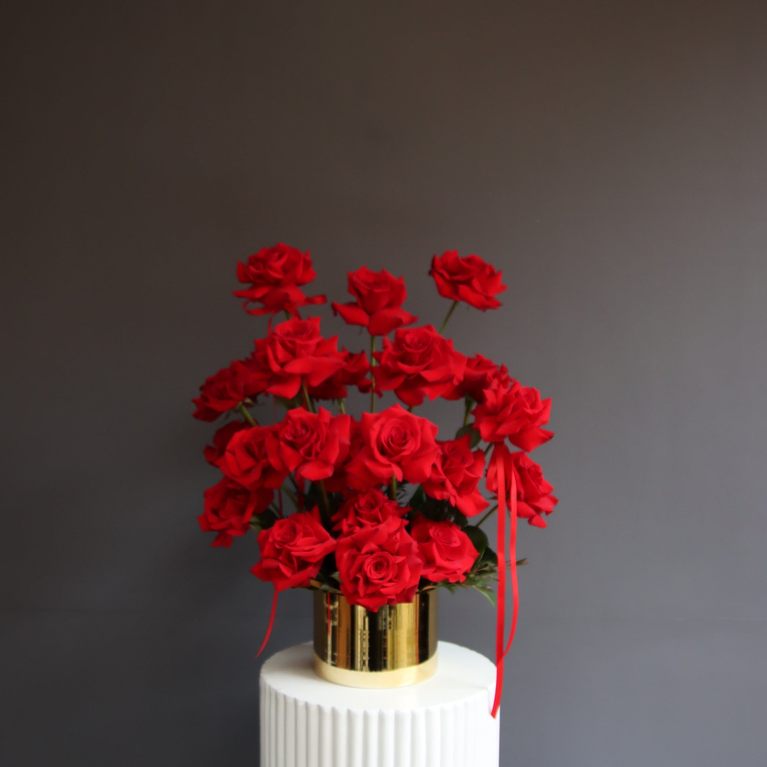 Red reflexed roses arranged in a gold glass pot