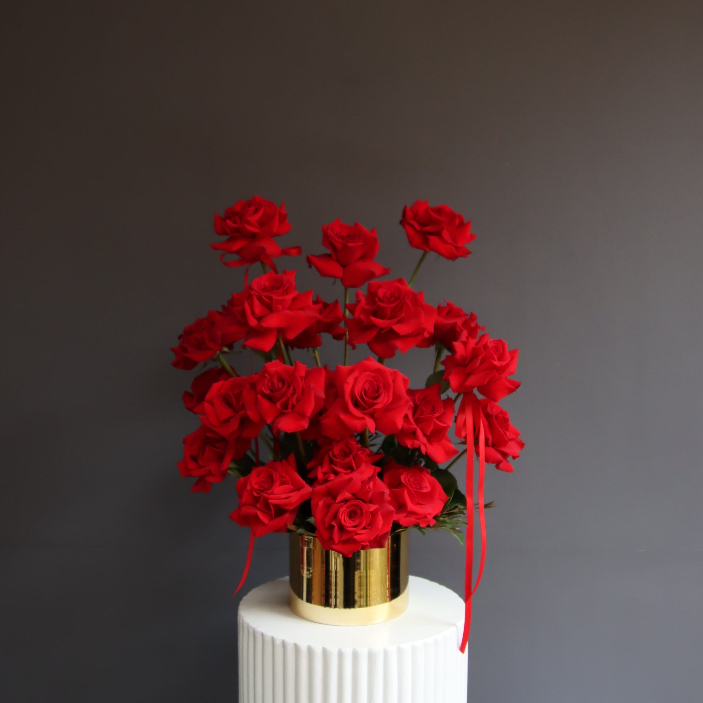 Red reflexed roses arranged in a gold glass pot