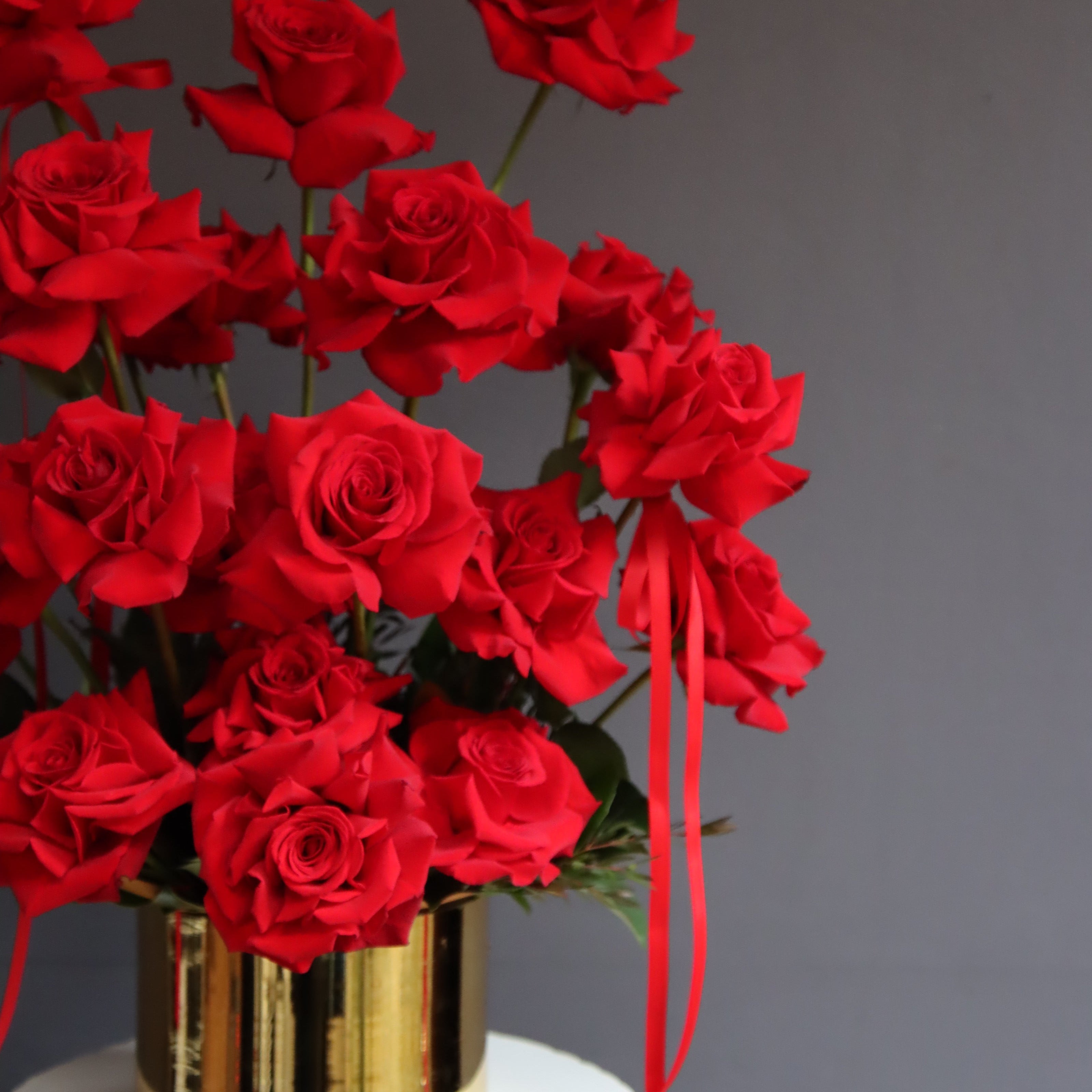 Red reflexed roses arranged in a gold glass pot