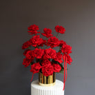 Red reflexed roses arranged in a gold glass pot