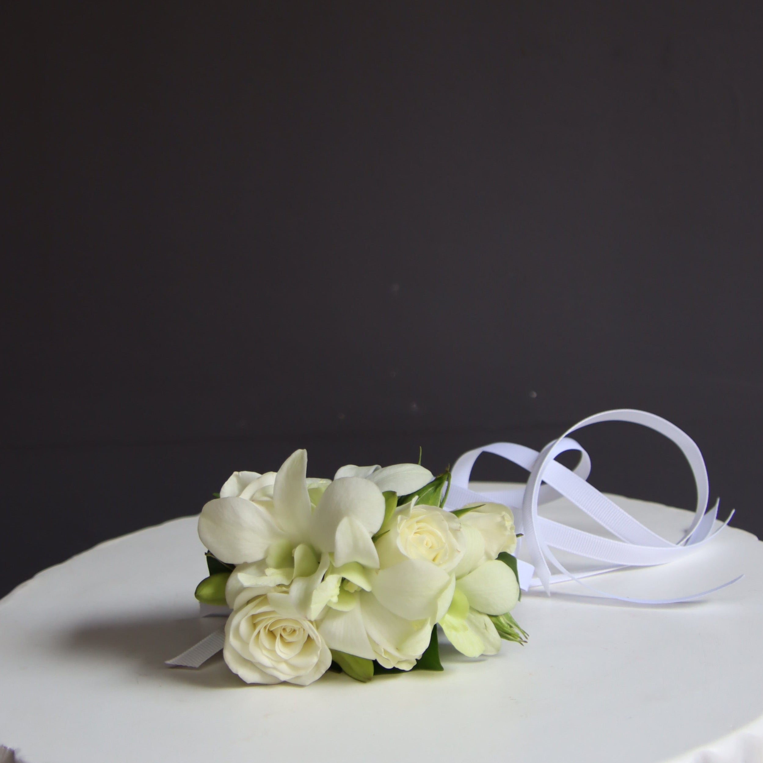 Our classic delicate fully wired wrist corsage features white spray roses and white dendrobium orchids with buds, accented with minimal greenery and ribbons. The wired design wraps securely around the wrist like a watch, ensuring it stays in place throughout your event. Ideal for weddings, formals, and special occasions. Available in a range of colors to complement your outfit or event theme.